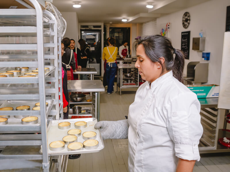 A baker taking a tray of pastry cases from a proving rack